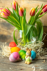 Easter eggs, bunny and spring yellow-orange tulips on a raw, rustic, wooden background