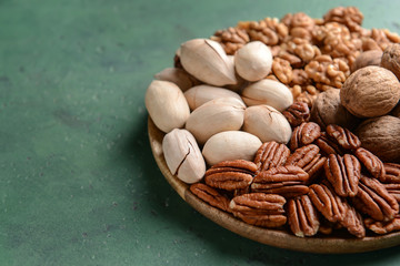 Plate with walnut and pecan nuts on color background