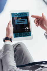 partial view of businessman using digital tablet with booking application on screen