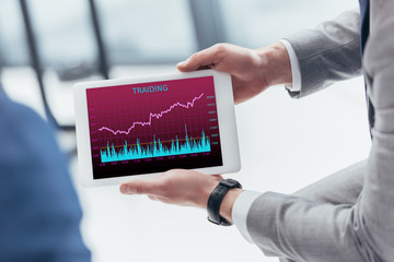 partial view of businessman holding digital tablet with trading graphs on screen