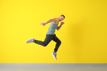 Young male dancer jumping near color wall