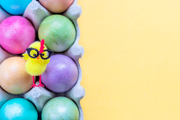 Multicolored easter eggs in a box with cute yellow chick. Top view on pastel orange background.