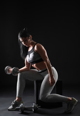 Fototapeta na wymiar Sporty muscular woman with dumbbell on dark background