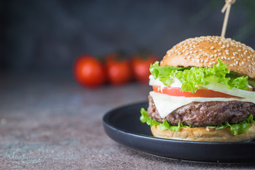 Hamburger with beef meat burger and fresh vegetables on dark background. Tasty fast food.