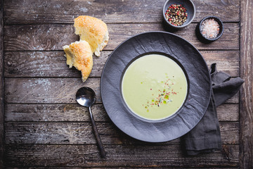 Broccoli cream soup in dark bowl on wooden background, top view