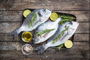 Fresh raw Dorado or sea bream with spices, herbs, lemon and salt over wooden background Top view