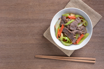 top view of stir fried beef with banana pepper in a ceramic bowl on wooden table. hot and spicy homemade style food concept.