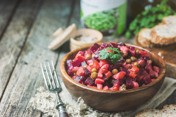 Russian beetroot salad vinaigrette in wooden bowl with rye bread, rustic background