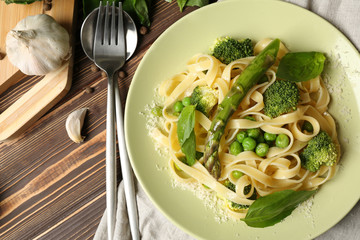 Plate with tasty pasta and green vegetables on wooden table