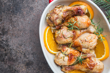 Baked chicken drumstick in a dish with orange and rosemary, top view