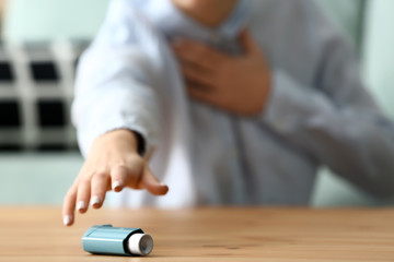 Fototapeta premium Young woman with asthma attack taking inhaler from table, closeup