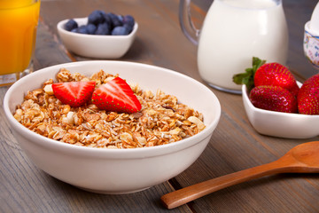 A plate with muesli, strawberries, juice, honey and milk on a white background.