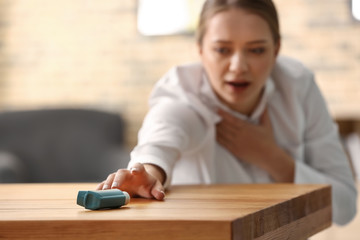 Young woman with asthma attack taking inhaler from table - obrazy, fototapety, plakaty