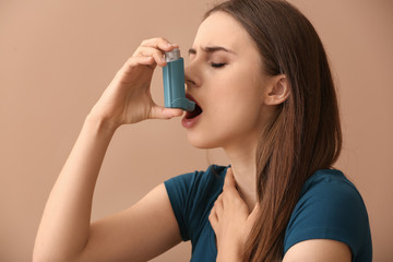 Young woman with inhaler having asthma attack on color background