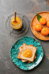 Jar of tasty tangerine jam with toasted bread on grey table