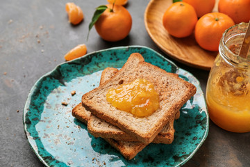 Plate with toasted bread and tasty tangerine jam on grey table