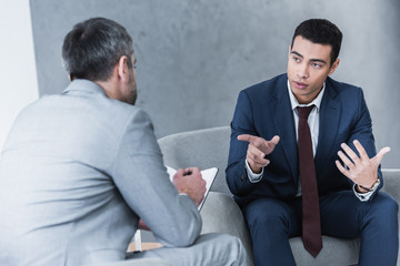 young businessman talking and looking at business mentor sitting and taking notes in notebook