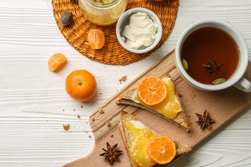 Tasty bread with butter, tangerine jam and cup of tea on wooden table