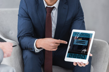 cropped shot of businessman in formal wear pointing with finger at digital tablet with booking app