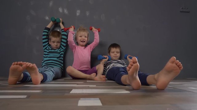 Cheerful children in multi-colored striped clothes are engaged in gymnastics with dumbbells. Legs and feet close-up. Children enjoy winter vacations together. Concept of family fitness classes.