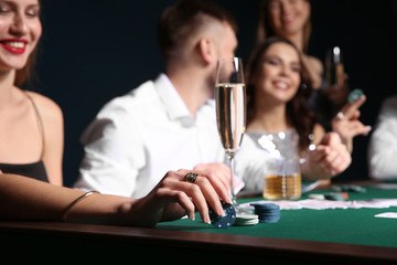 Woman with glass of champagne sitting at table with people playing poker in casino