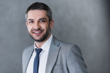 portrait of handsome businessman in formal wear smiling at camera on grey