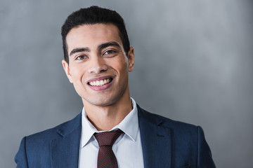 portrait of handsome young businessman smiling at camera on grey