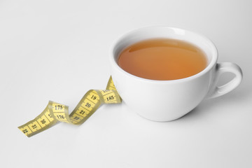 Cup of tea with measuring tape on white background. Weight loss concept