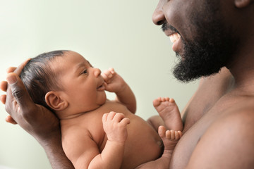 Happy African-American father with little baby on color background