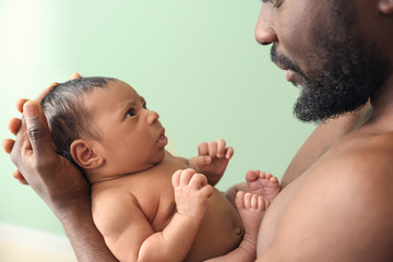 Happy African-American father with little baby on color background