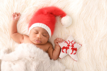 Cute African-American baby in Santa Claus hat sleeping on white furry plaid
