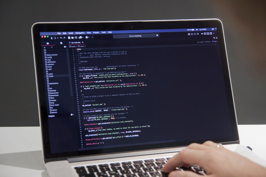 Male Programmer Working On Laptop Computer At White Desk In Office