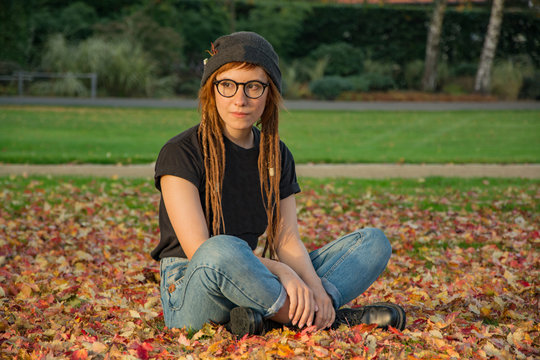 young womnan with red dreadlocks amd glasses relaxing in the autumn park 