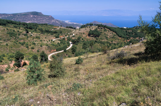Greek Mediterranean landscape in the mountains on summer sunny day; The road as a serpentine goes to the blue sea