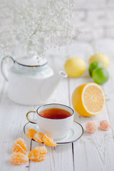 Obraz na płótnie Canvas Hot tea with fresh orange, lemon, lime, mandarin or tangerine lobules on a white wooden table. White porcelain teapot and cup. White flowers. 