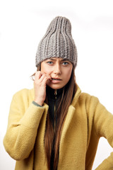 Confused and unhappy woman in colorful winter clothes holding a snowflake on the yellow background