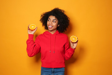 Portrait of young African-American woman with orange halves on color background