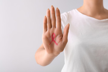 Woman with pink ribbon drawn on her palm against light background. Breast cancer awareness concept