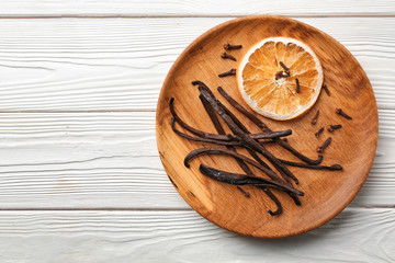 Plate with dry orange slice and aromatic vanilla sticks on white wooden background
