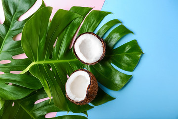 Coconut and tropical leaves on color background