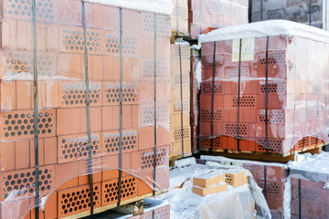 Stock pallets of red bricks wrapped in stretch film at wholesale outdoor market ot store. Construction site with prepared materials