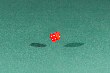 One red dice falling on a green table
