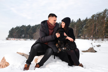 Young caucasian couple in love sitting on stone with dog on winter beach, embracing, enjoy the romantic moment,  feeling intimacy and closeness. Close up portrait of sensual girlfriend and boyfriend.