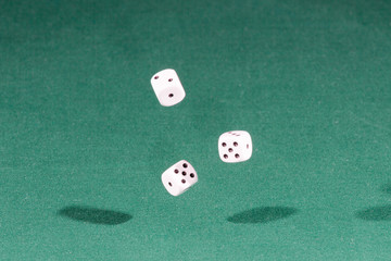 Three white dices falling on a green table