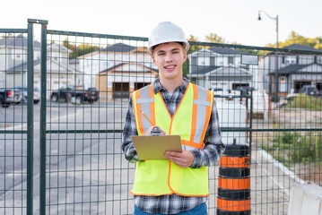Happy young construction worker wearing safety gear and holding a clipboard.