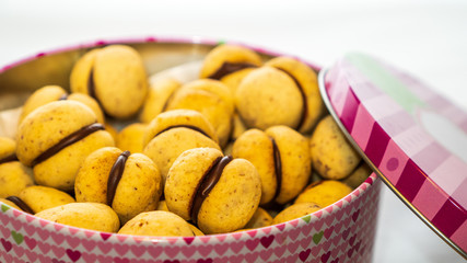 Closeup of Lady's Kisses (Baci di Dama), delicious Italian almond cookies with chocolate filling in a biscuits tin can on a white background.