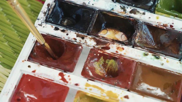 Closeup of paintbrush is dunks in watercolors paints set