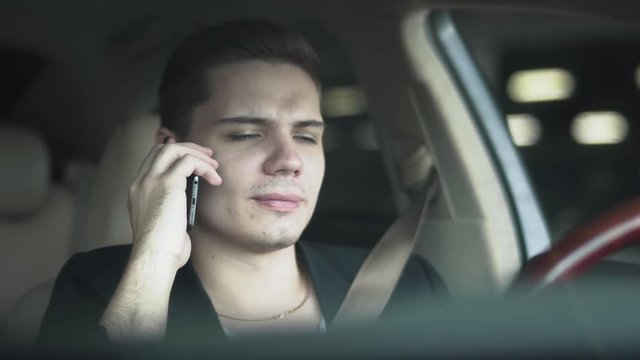 Portrait of a young man chewing gum and talking on a mobile phone in the car close-up
