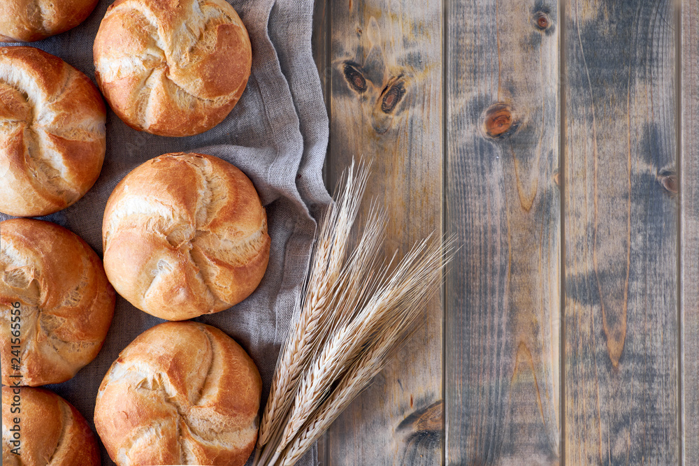 Wall mural crusty round bread rolls, known as kaiser or vienna rolls scattered on linen towel on rustic wood, f