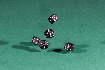 Five black dices falling on a green table